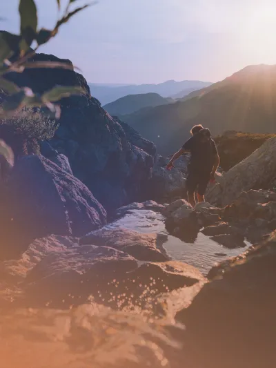 Mann som går tur i fjellet med stein og sol i bakgrunnen.