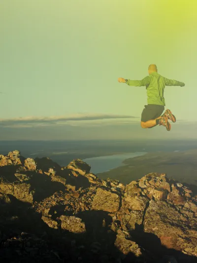 En mann som hopper på toppen av et fjell, han er ikledd grønnjakke.