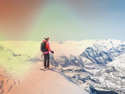 En dame som står på toppen av et snødekket fjell og er klar for å sette utfor, hun er ikledd.