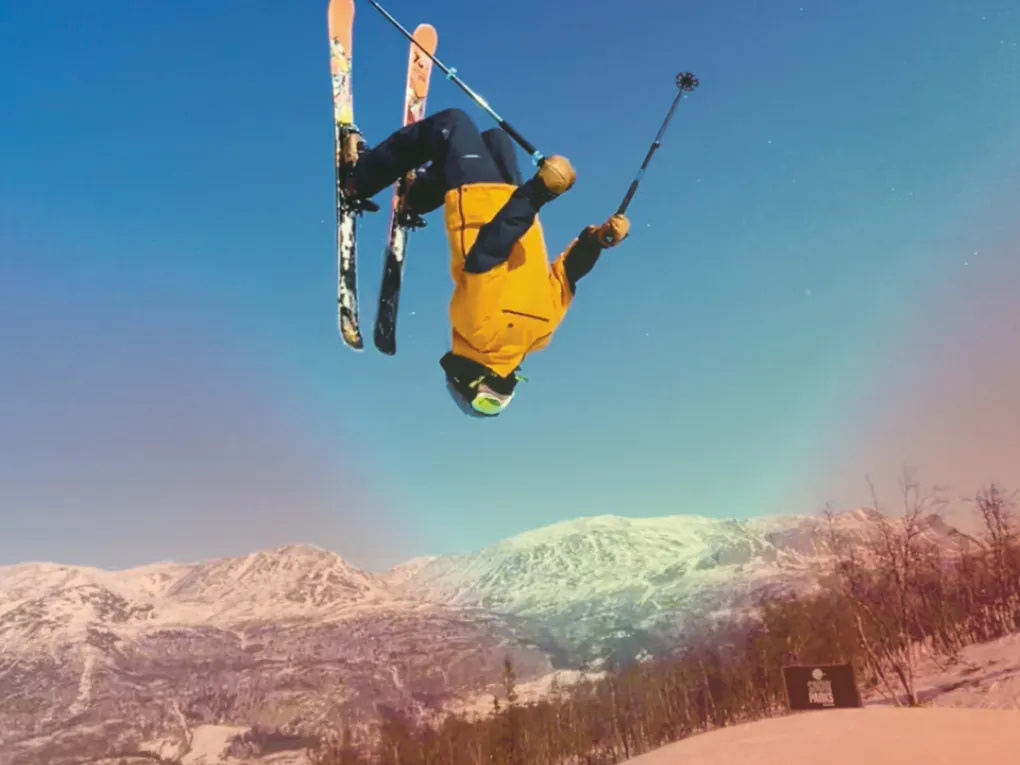 En mann som tar en backflip på ski, med gul jakke.